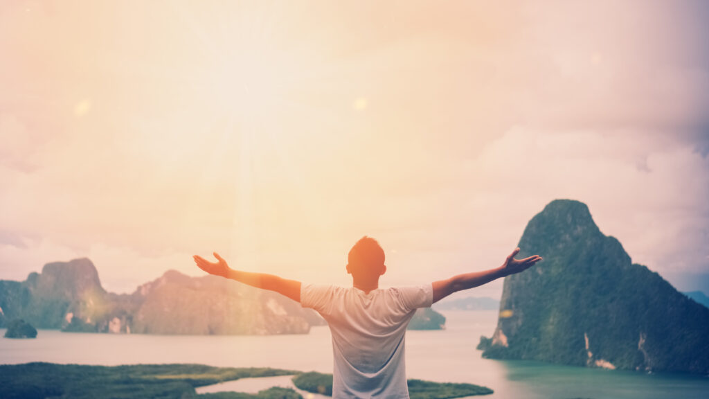 Feel good freedom and travel adventure concept. Copy space of happy man raise hands on  top of mountain with sun light abstract background. Vintage tone filter effect color style.